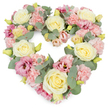 A full, heart-shaped funeral wreath is displayed against a spotless white background, its soft pastel palette and dense composition evoking gentle sympathy and enduring love. The heart is carefully shaped by rows of creamy ivory and light butter-yellow roses, each bloom richly petalled and slightly cupped, forming the main structure of the tribute. Tucked between these roses are generous tufts of pastel pink carnations, their fine, ruffled petals blurring the edges and giving the design a feathery, comforting feel. Accents of darker pink and mauve lisianthus are scattered throughout, their more open, trumpet-like blooms adding depth and a slightly richer note of colour, much like the subtle variations you notice walking through the landscaped areas near King George V Playing Fields in Stevenage. Woven among the blossoms are soft stems of eucalyptus, their rounded, silvery-green leaves leaning gently away from the flowers, bringing coolness and a whisper of woodland fragrance to the imagined scene. Tiny yellow-green buds dot the arrangement, signifying freshness and the ongoing cycle of life, even at a moment of farewell. Every inch of the heart is filled, creating a plush, velvety surface that feels protective and embracing, rather than sparse or fragile. This type of arrangement would be chosen by families in Stevenage who want their floral tribute at a funeral or memorial to speak quietly but clearly of love, remembrance, and gratitude, offering a visual expression of comfort when words may be hard to find.